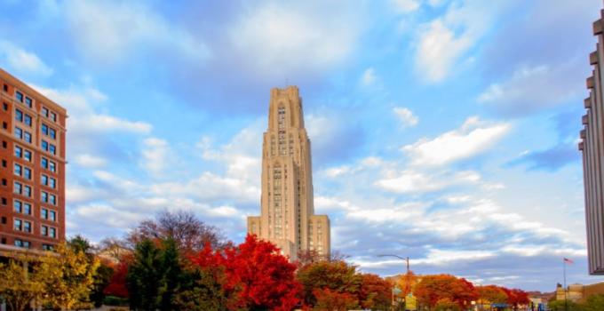 cathedral of learning against a blue sky with puffy clouds and trees with red leaves